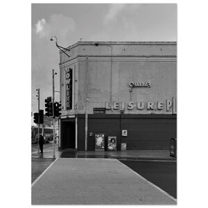 May include: Black and white photograph of a building with the words "BOWLING" and "LEISURE" in large letters. The building has a retro aesthetic, with a cloudy sky overhead. A crosswalk and traffic lights are in the foreground.