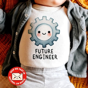 May include: A white baby onesie with a blue gear graphic and the text "FUTURE ENGINEER". The onesie is worn with a gray cardigan and gray pants. The background includes a yellow blanket.
