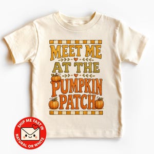 Peut inclure: Un t-shirt à manches courtes de couleur crème avec une impression graphique portant le texte "MEET ME AT THE PUMPKIN PATCH" en lettres orange et jaunes, accompagné d'illustrations de trois citrouilles orange et de petits cœurs orange.