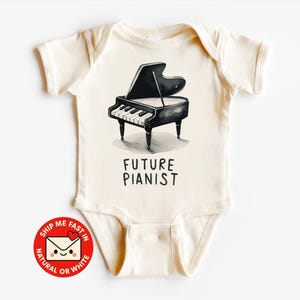 Può includere: Body da bambino color crema con un'illustrazione in bianco e nero di un pianoforte a coda. Il testo "FUTURE PIANIST" è stampato sotto. Il body ha maniche corte e chiusura con bottoni a pressione.