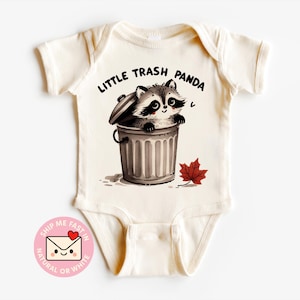 May include: Cream-colored baby bodysuit with the text "LITTLE TRASH PANDA" above a cartoon raccoon peeking out of a trash can. A red maple leaf is next to the trash can. The bodysuit has short sleeves.
