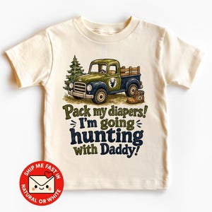 Könnte beinhalten: Ein cremefarbenes Kurzarm-T-Shirt mit einer Grafik eines grünen und blauen Vintage-Pickups, einer Tanne und einem braunen Stiefel. Der Text lautet: Pack my diapers! I'm going hunting with Daddy! Das Design enthält ein Hirsch-Silhouette-Logo.