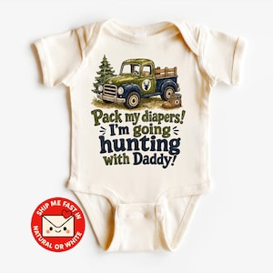 Könnte beinhalten: Ein cremefarbener Kurzarm-Babybody mit einer Grafik eines grünen und blauen Vintage-Pickups, einer Tanne und einem braunen Stiefel. Der Text lautet: Pack my diapers! I'm going hunting with Daddy! Das Design enthält ein kleines Hirsch-Emblem.