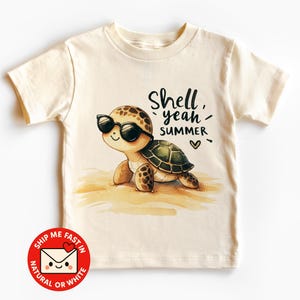Könnte beinhalten: Cremefarbenes T-Shirt mit einer Cartoon-Schildkröte mit Sonnenbrille. Die Schildkröte befindet sich an einem Sandstrand mit den Worten "Shell yeah, SUMMER" in schwarzer Schrift. Ein rot-weißer Aufkleber mit dem Text "Ship me fast in natural or white" befindet sich unten.