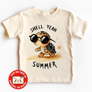 Könnte beinhalten: Cremefarbenes T-Shirt mit einer Cartoon-Schildkröte mit Sonnenbrille. Die Schildkröte befindet sich an einem Sandstrand mit den Worten "SHELL YEAH SUMMER" darüber und darunter. Das T-Shirt hat kurze Ärmel.