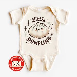Könnte beinhalten: Cremefarbener Baby-Body mit einem niedlichen Knödel-Motiv. Das Motiv enthält den Text "Little DUMPLING" und eine lächelnde Knödel-Figur. Der Body hat kurze Ärmel und einen Druckknopfverschluss.