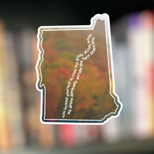 May include: A sticker in the shape of a state with a white border. The sticker has a colorful, textured background with text that reads "You inched yourself across the great divide while we drove aimlessly across the Twin State line."