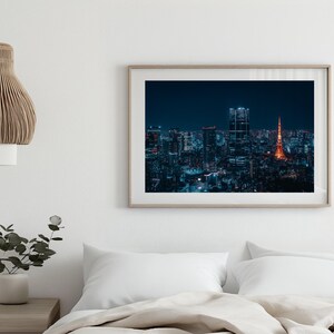 May include: A framed photograph of a nighttime cityscape, showcasing a vibrant skyline with illuminated buildings and a prominent orange tower. The image is set against a dark blue sky, creating a striking contrast.