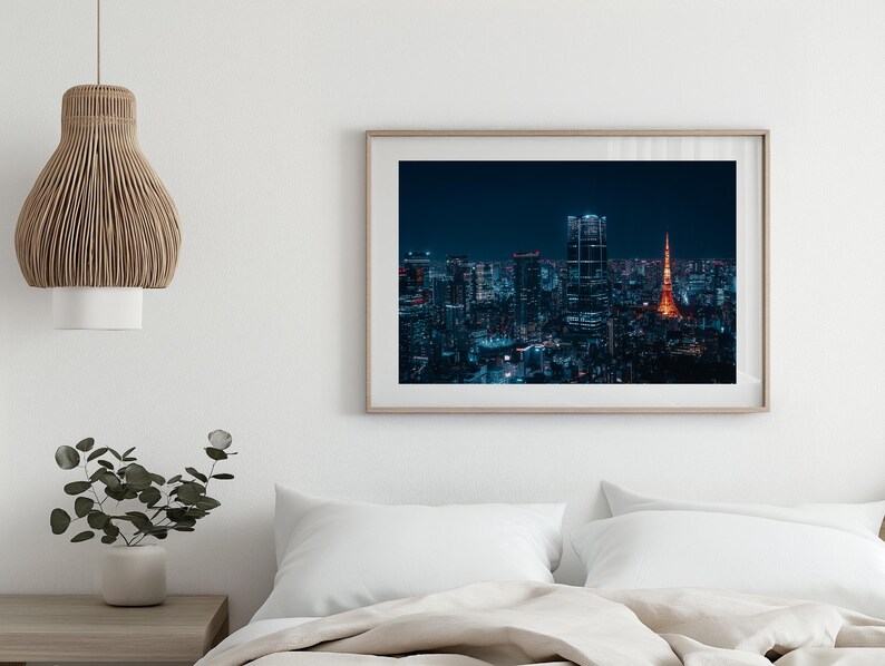 May include: A framed photograph of a nighttime cityscape, showcasing a vibrant skyline with illuminated buildings and a prominent orange tower. The image is set against a dark blue sky, creating a striking contrast.