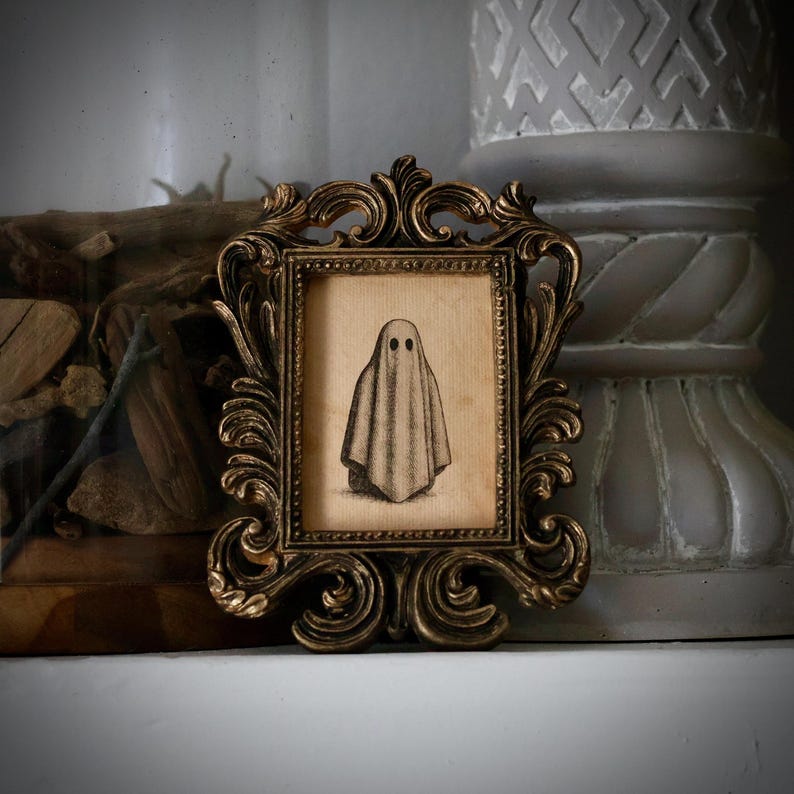 Peut inclure: Une petite impression encadr&eacute;e d'un fant&ocirc;me. L'&oelig;uvre d'art est dans un cadre dor&eacute; orn&eacute;. Le fant&ocirc;me est repr&eacute;sent&eacute; comme un drap&eacute; avec deux trous noirs pour les yeux. Le cadre a un design baroque antique.