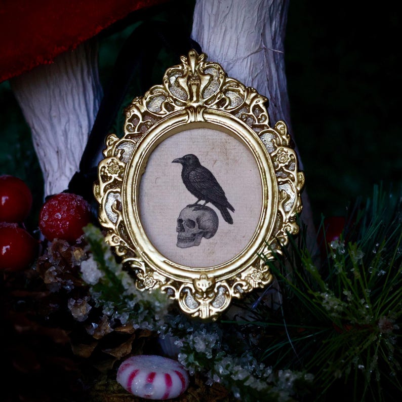 May include: A framed print featuring a black raven perched atop a skull. The print is set within an ornate, gold-colored oval frame. The background includes red berries, pine needles, and a candy cane.