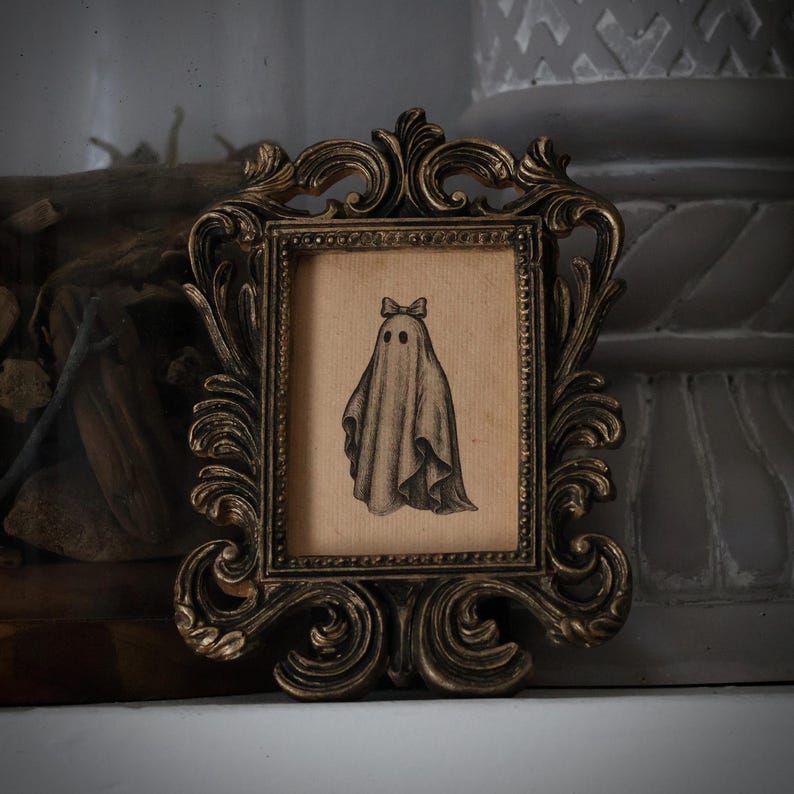 Peut inclure: Illustration encadr&eacute;e d'un fant&ocirc;me portant un n&oelig;ud. L'&oelig;uvre d'art est dans un cadre de style vintage avec des d&eacute;tails orn&eacute;s. Le fant&ocirc;me est repr&eacute;sent&eacute; dans un drap&eacute; avec deux trous pour les yeux et un n&oelig;ud. Le cadre a une finition bronze.
