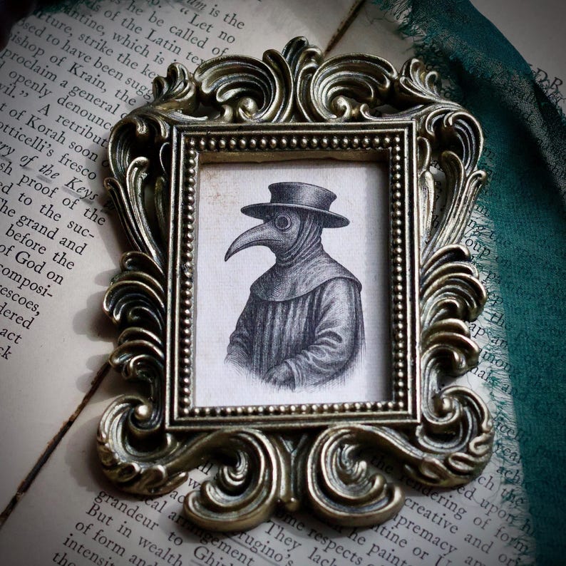 May include: A framed pencil sketch of a plague doctor in a decorative gold-colored frame. The artwork depicts the plague doctor wearing a hat and a long-beaked mask. The frame has ornate scrollwork.