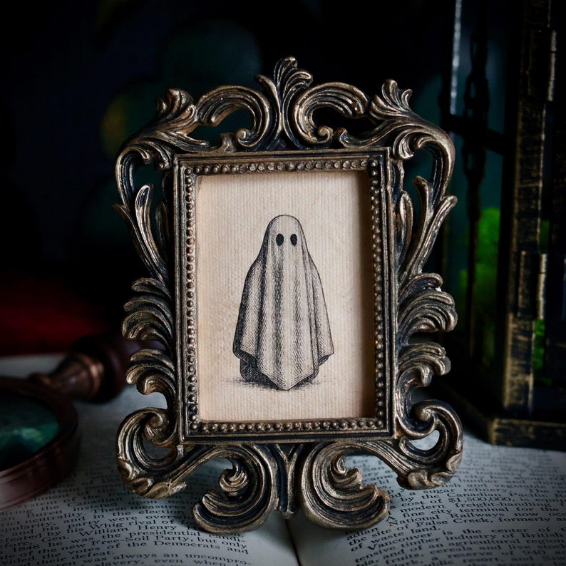Peut inclure: Une impression encadr&eacute;e de style vintage repr&eacute;sentant un fant&ocirc;me simple. L'&oelig;uvre d'art est en noir et blanc sur un fond beige, dans un cadre dor&eacute; antique orn&eacute; de volutes d&eacute;taill&eacute;es.