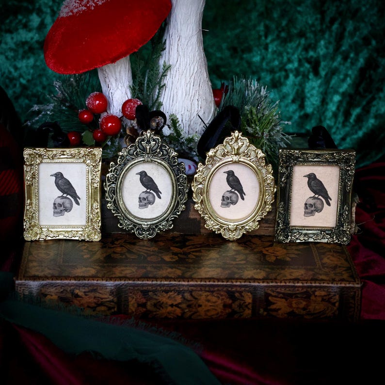 May include: Four ornate picture frames in gold and dark metal tones. Each frame holds a print of a black raven perched on a skull. The frames are arranged on a decorative, antique-style box, with a festive background.