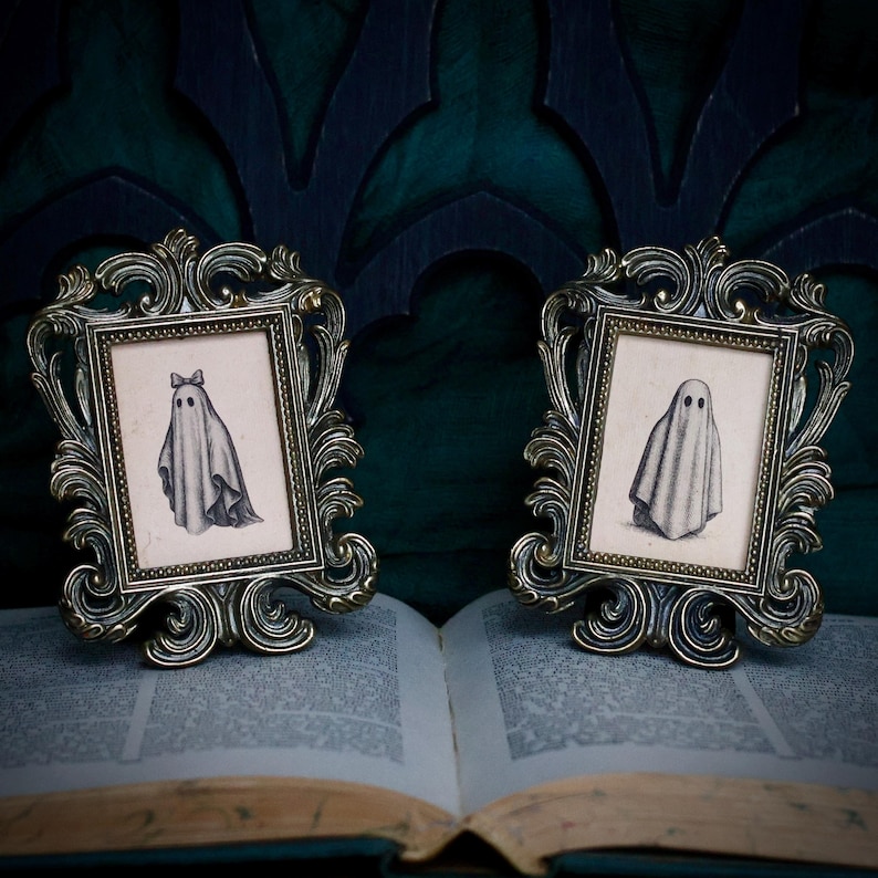 Peut inclure: Deux cadres dor&eacute;s anciens avec des d&eacute;tails orn&eacute;s. Chaque cadre contient une petite illustration en noir et blanc d'un fant&ocirc;me. Les cadres sont pos&eacute;s sur un livre ouvert aux pages vieillies, sur fond vert fonc&eacute;.