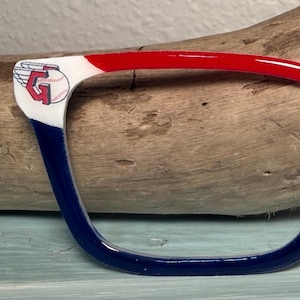 Puede incluir: Montura de gafas en rojo, blanco y azul, con un logotipo temático de béisbol. Las monturas tienen un acabado brillante. El logotipo de béisbol está en la esquina de la montura.