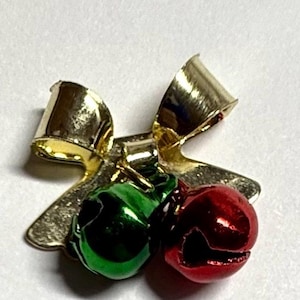 May include: A gold-coloured metal bow with two small bells. One bell is green, and the other is red. The bells are attached to the bow with a small metal piece. The bow has a shiny finish.