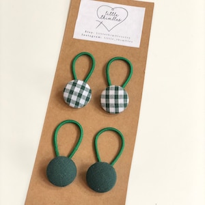 May include: Four green and white gingham fabric covered buttons with green elastic loops, and two solid green fabric covered buttons with green elastic loops, displayed on a brown card. The card has a white label with the text "little thimbles".