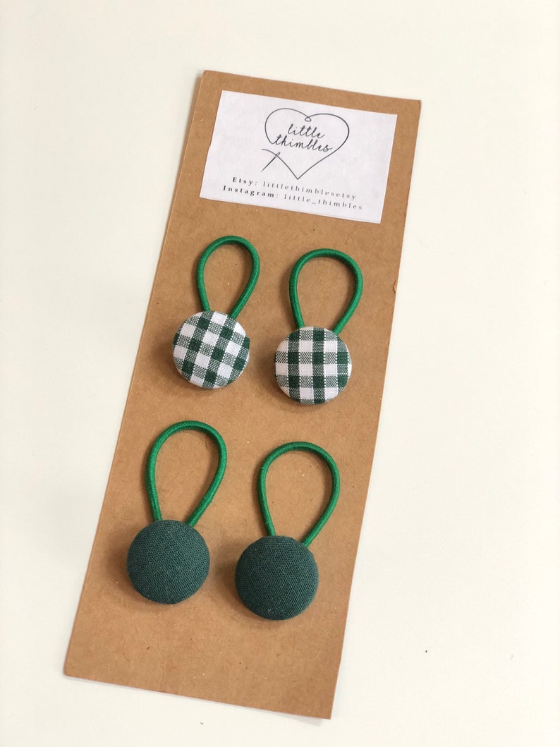 May include: Four green and white gingham fabric covered buttons with green elastic loops, and two solid green fabric covered buttons with green elastic loops, displayed on a brown card. The card has a white label with the text "little thimbles".