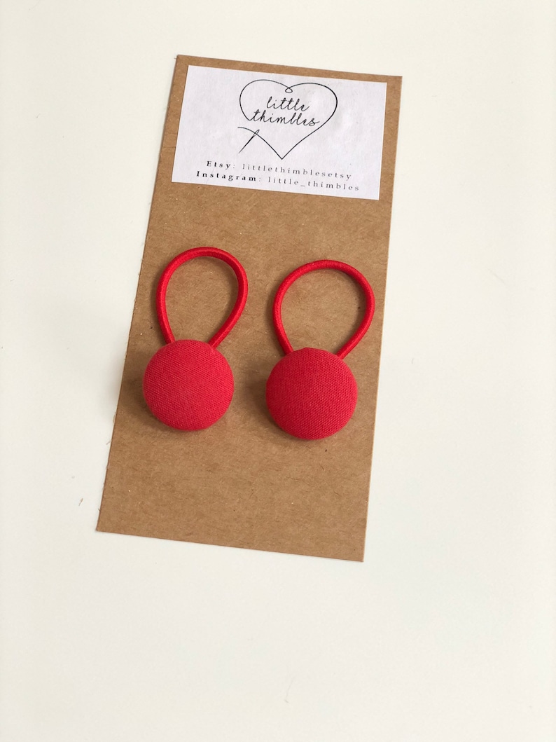 May include: Two red fabric-covered button earrings with elastic loops. The earrings are attached to a brown card with the text "little thimbles" and Etsy and Instagram account information.