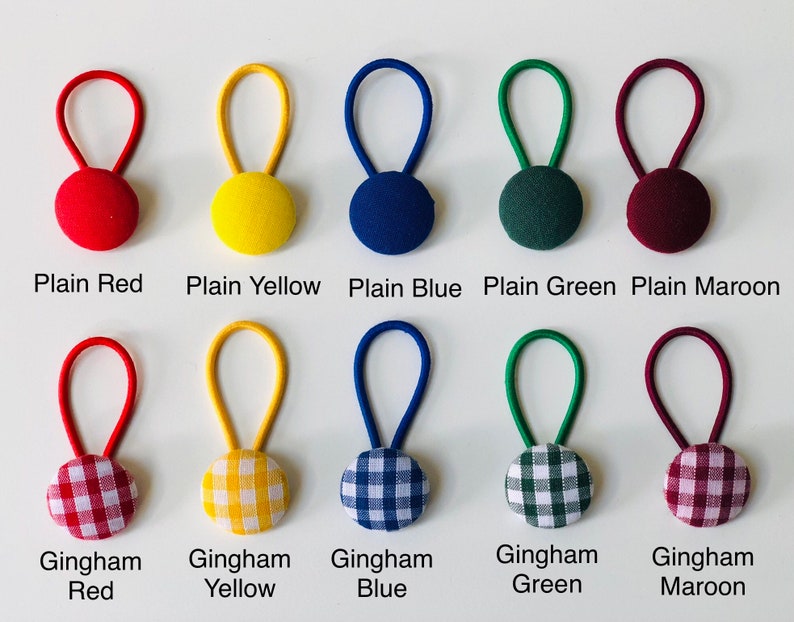 May include: A collection of ten fabric-covered button hair ties in various colors and patterns. The top row features solid colors: red, yellow, blue, green, and maroon. The bottom row displays gingham patterns in red, yellow, blue, green, and maroon. Each tie has a loop.
