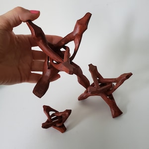 May include: A collection of four handcrafted, dark brown wooden stands. The stands have a tripod design with three legs and a central support structure. The wood has a natural grain and a smooth finish. The stands vary in size.