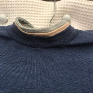 May include: A navy blue long-sleeved shirt with a beige and gray striped collar.