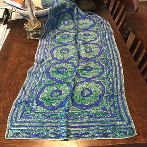 May include: A blue and green patterned silk scarf with a white background. The pattern features stylised flowers and a border of repeating geometric shapes. The scarf is approximately 114 cm long and 46 cm wide.