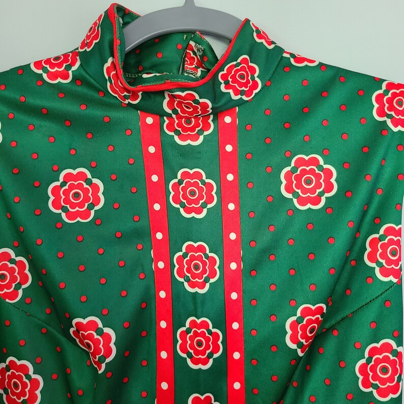 Pu&ograve; includere: Un vestito a fantasia verde e rossa con collo alto e corpetto aderente. Il vestito ha un motivo a righe rosse e bianche sul davanti e un motivo a pois rossi sul resto del vestito.