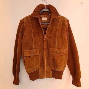 May include: A brown suede jacket with a knit collar, cuffs, and waistband. The jacket has a zipper closure and two flap pockets.