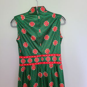 Pu&ograve; includere: Un abito verde senza maniche con un motivo floreale rosso e bianco. L'abito ha un collo alto e un corpetto aderente. La gonna &egrave; ampia e fluida.