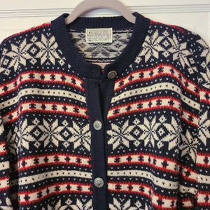 May include: A navy blue cardigan with a white and red snowflake pattern. The cardigan has a button closure and is made of wool. The label reads "Pendleton" and "Made in USA".