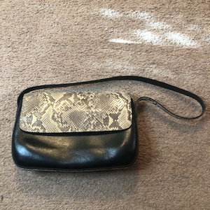 Peut inclure: Un sac à main en cuir noir avec un rabat en peau de serpent. Le sac a une longue bandoulière.