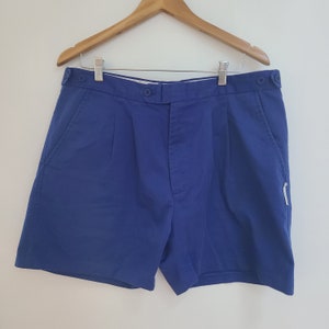 May include: A pair of blue shorts with pleats and a button fly. The shorts have two pockets on the front and a small pocket on the right side.