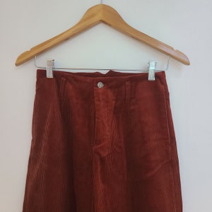 Op de afbeelding: Een broek van roestkleurige corduroy met een knoopsluiting en een rechte pijp.