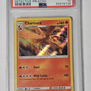 May include: A graded Pok&eacute;mon card featuring Charizard from the 2019 Sun & Moon set. The card is encased in a protective holder and has a holographic design. The card's text includes "Charizard" and "Detective Pikachu".