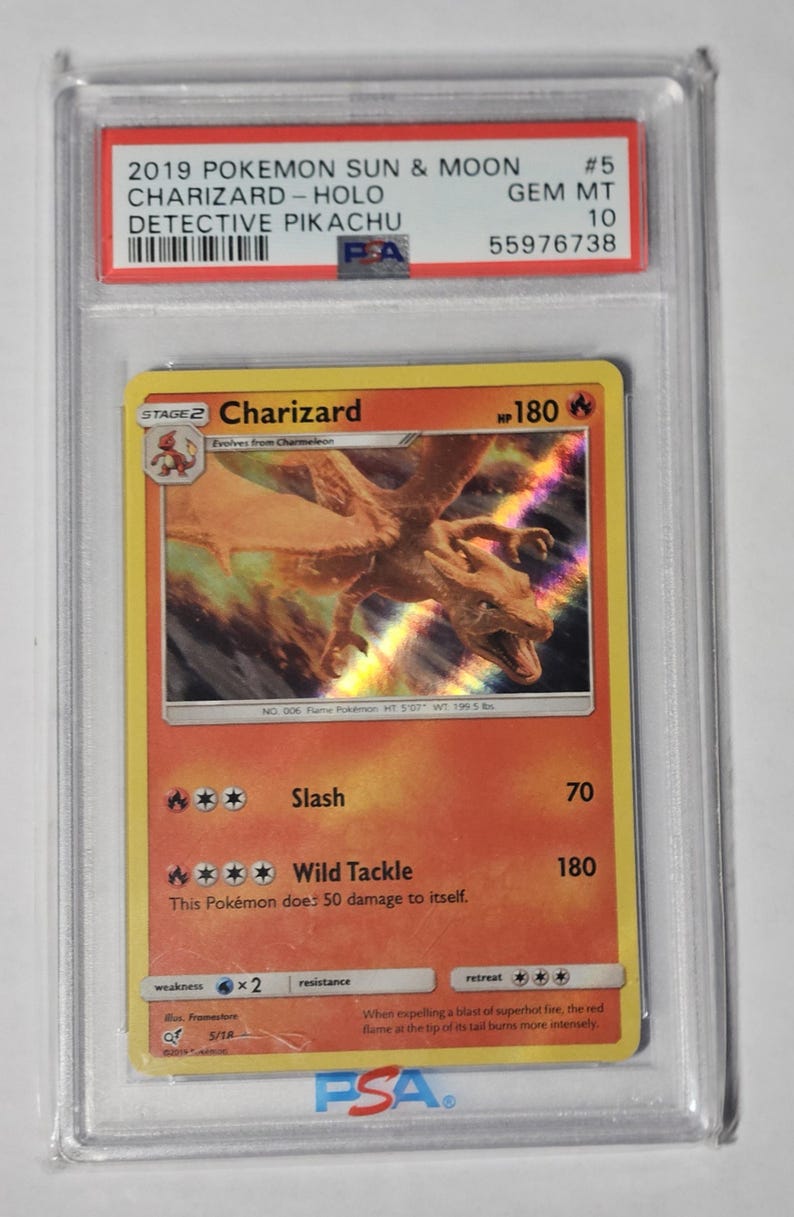 May include: A graded Pok&eacute;mon card featuring Charizard from the 2019 Sun & Moon set. The card is encased in a protective holder and has a holographic design. The card's text includes "Charizard" and "Detective Pikachu".