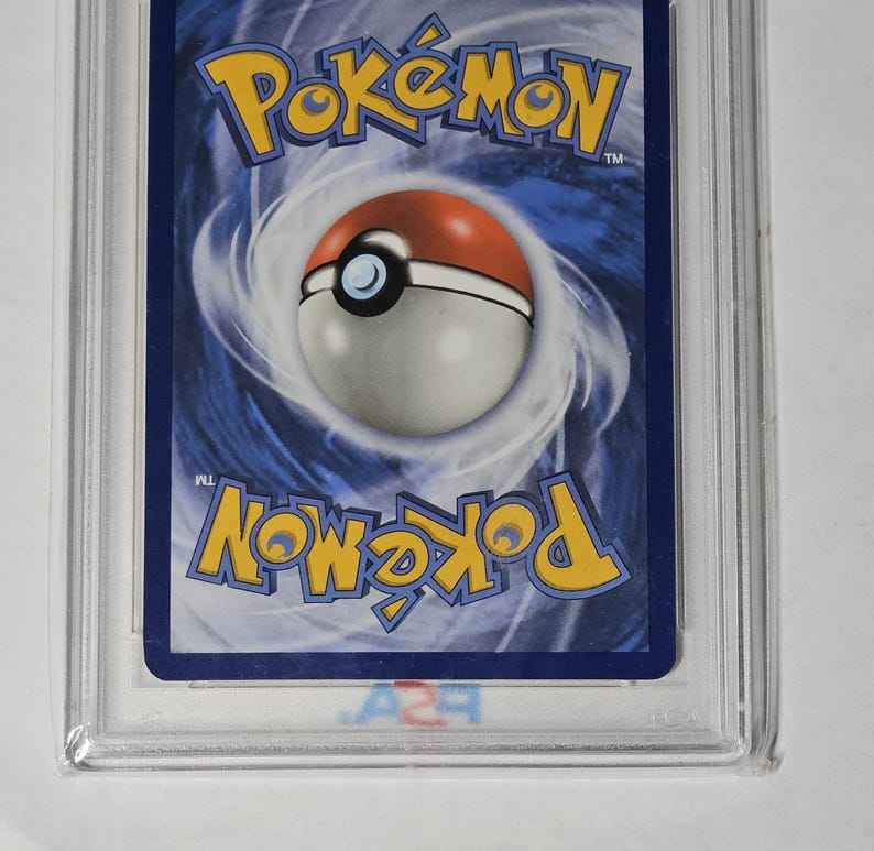 May include: A graded Pok&eacute;mon trading card, encased in a clear plastic holder. The card's back features a blue background with the Pok&eacute;mon logo in yellow and a Pok&eacute; Ball design. The card is in a protective case.