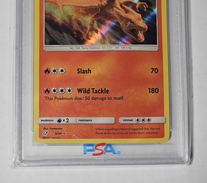 May include: A graded Pok&eacute;mon trading card featuring Charizard. The card has a red and orange background with the image of a dragon-like creature. Text includes "Slash" and "Wild Tackle" with damage values. The card is encased in a protective holder.