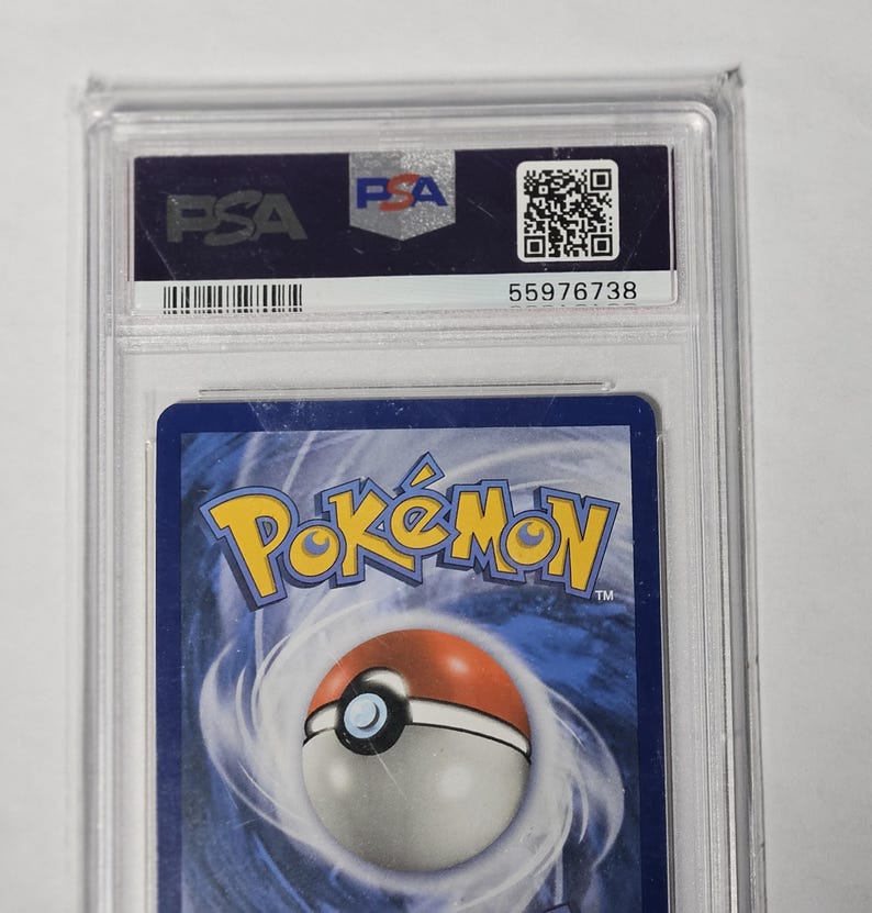 May include: A graded Pok&eacute;mon trading card encased in a clear plastic holder. The holder has a PSA label with a barcode and serial number. The card's back features the Pok&eacute;mon logo and a Pok&eacute; Ball design.