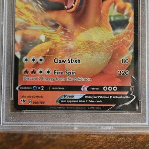 Puede incluir: Una carta coleccionable Pok&eacute;mon Charizard V, en un protector. La carta presenta una ilustraci&oacute;n naranja y amarilla de Charizard. El texto incluye "Claw Slash", "Fire Spin" y "V rule".