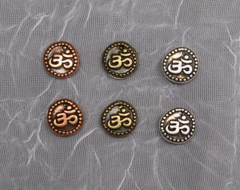 May include: Six metal charms with the Om symbol in different finishes. The charms are silver, gold, and copper.