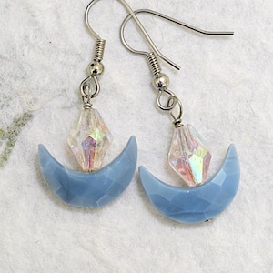 May include: A pair of silver dangle earrings with a blue crescent moon charm and a clear iridescent crystal bead.