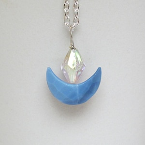 May include: A silver chain necklace with a blue crescent moon pendant and a clear iridescent crystal.