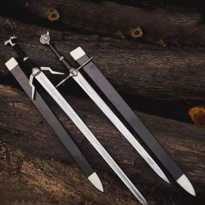 May include: Two steel swords with black grips and silver crossguards, each accompanied by a black scabbard with silver-toned metal fittings at the tip and throat. The pommels feature distinct silver emblems, one shaped like a wolf head.
