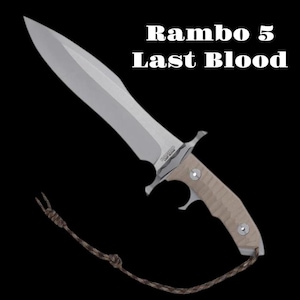 May include: A large, silver knife with a light brown handle and a lanyard. The text "Rambo 5 Last Blood" is displayed above the knife. The knife has a wide blade and a pointed tip.