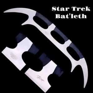Könnte beinhalten: Ein Star Trek Bat'leth, eine klingonische Waffe, wird vor schwarzem Hintergrund gezeigt. Das Bat'leth ist ein gebogenes Doppelklingenschwert mit silberner Klinge und schwarzem Griff. Zwei zusätzliche Klingen sind ebenfalls abgebildet.