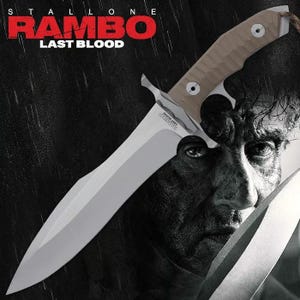 May include: A large, silver blade knife with a beige handle. The knife has a prominent guard and a partially serrated edge. The text "RAMBO LAST BLOOD" is visible on the blade and above the knife. The background is a black and white image of a man's face.