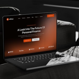 May include: A black laptop displaying a website with the text "A Look Into The Future Of Personal Finance." The website has an orange and white color scheme. The laptop is on a dark gray couch.